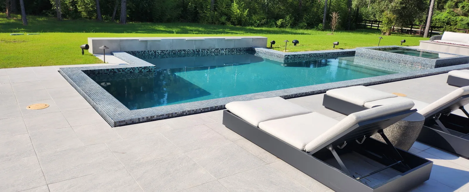 Modern pool and spa with dark glass mosaic tile and large-format stone deck