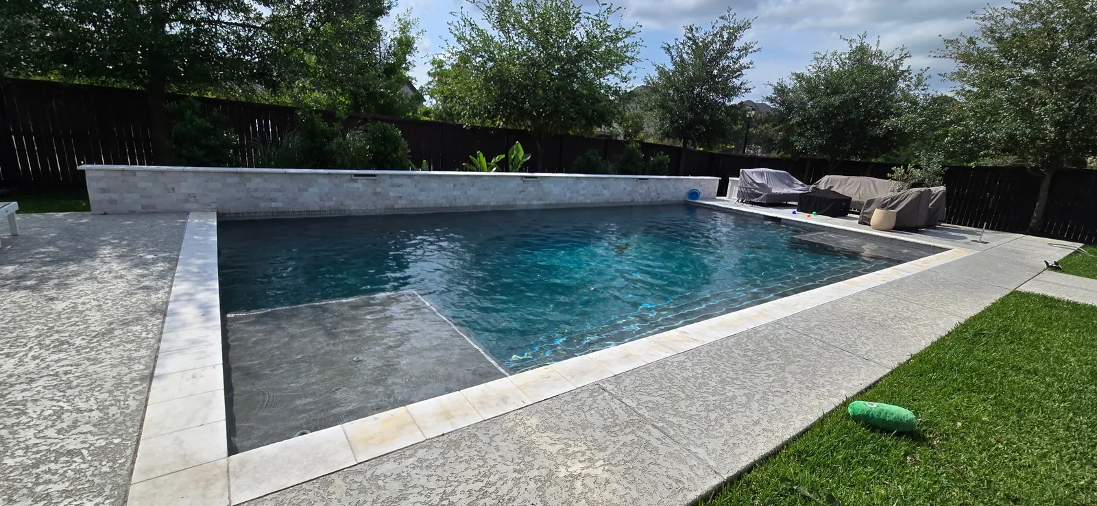 Rectangular pool with a stacked stone water wall and travertine coping
