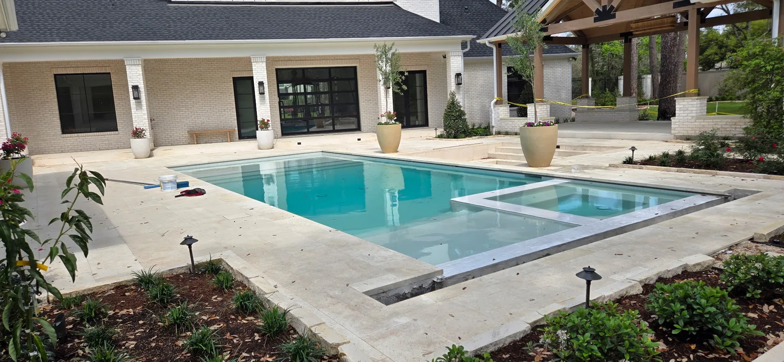 Rectangular pool and raised spa with travertine decking beside a Houston-area home