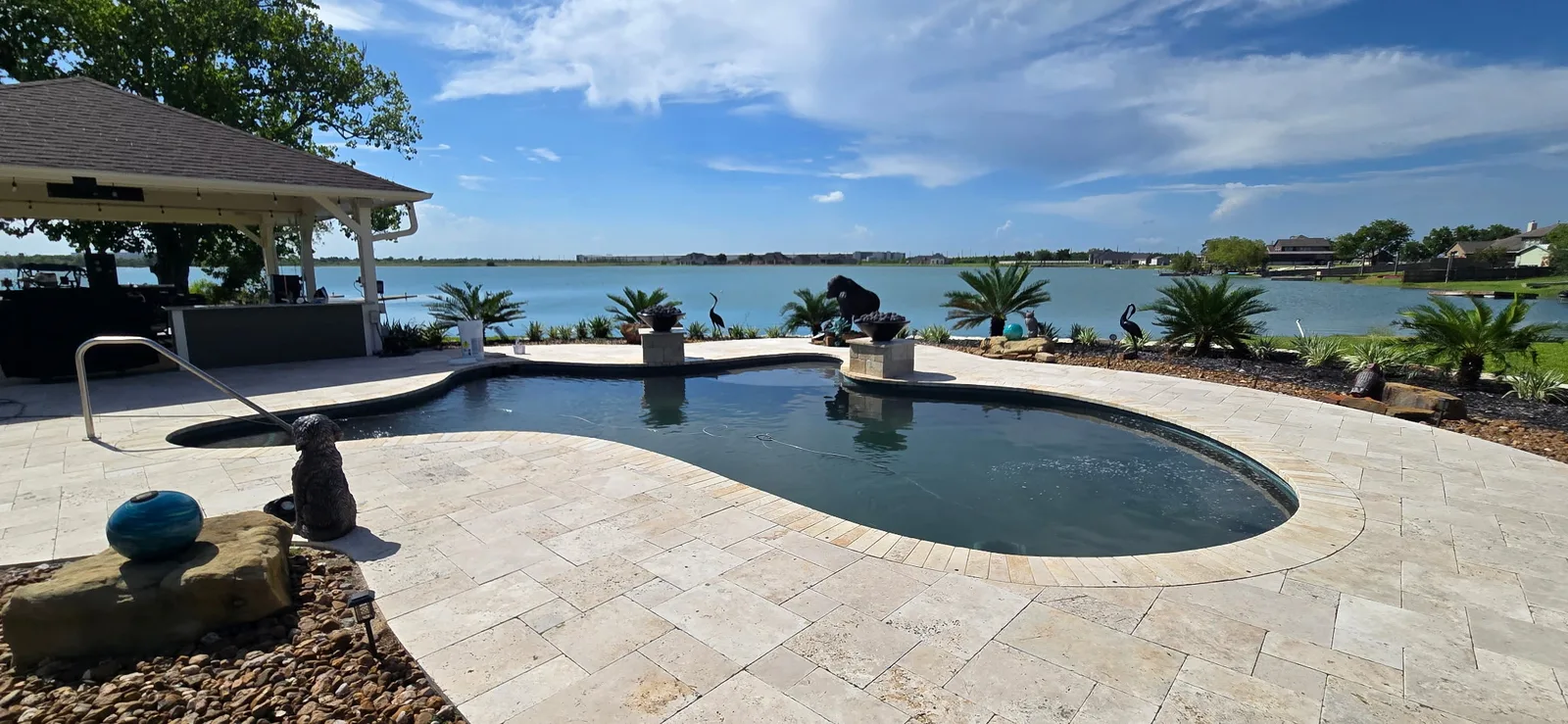 Freeform lakefront pool with travertine decking and fire bowls in the Greater Houston area